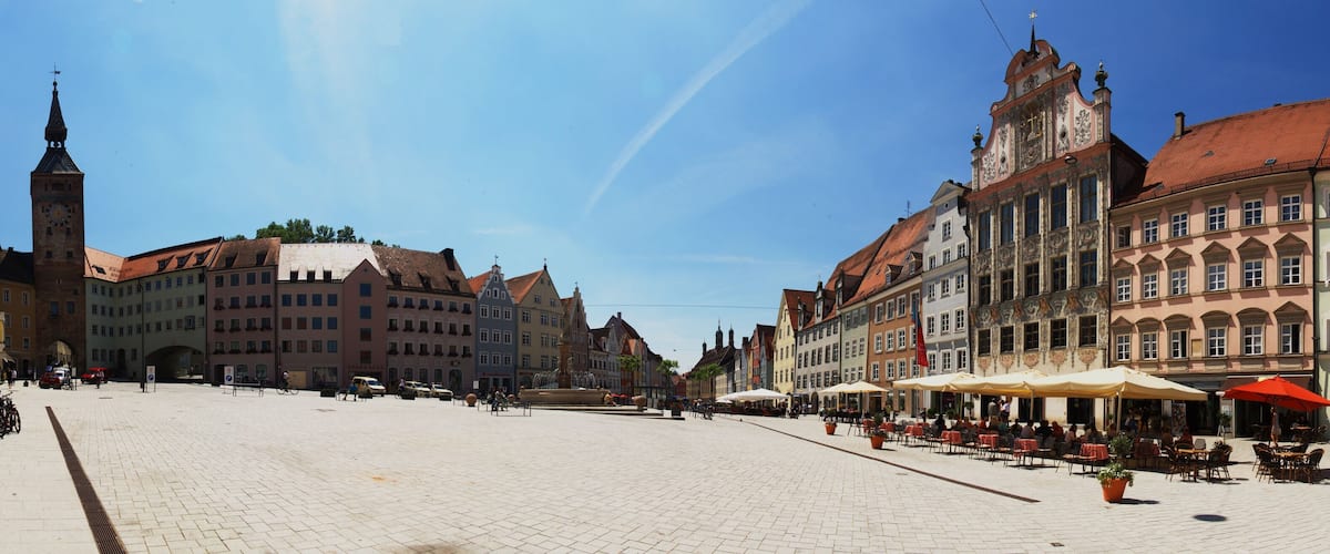 A cobblestone square with historic buildings, a clock tower, and outdoor seating areas.