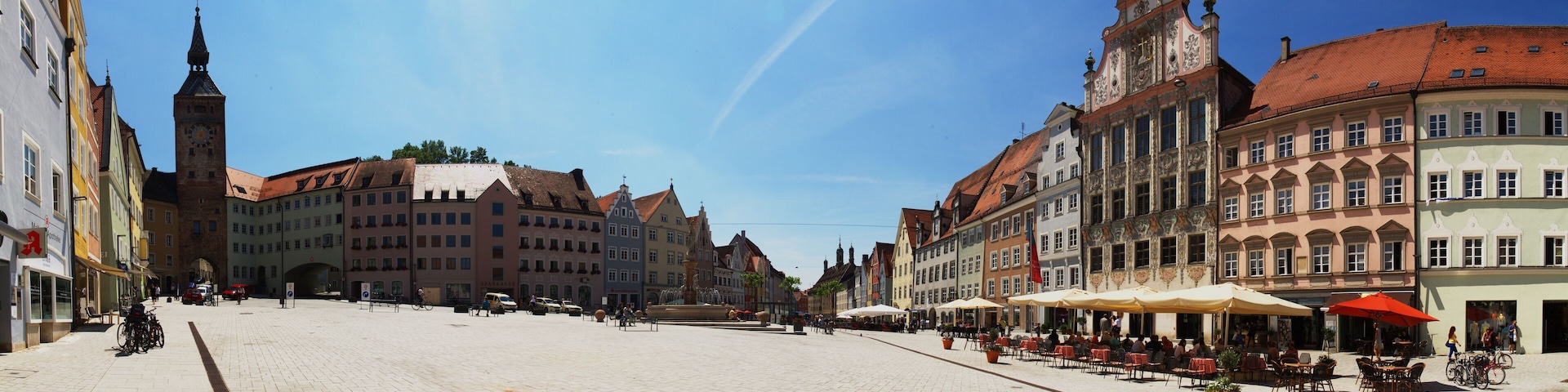 A cobblestone square with historic buildings, a clock tower, and outdoor seating areas.