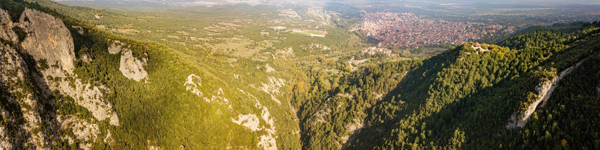 Aerial drone panoramic view of deep gorge and rocky ridge near Mountain Olympus and Litochoro village in the distance