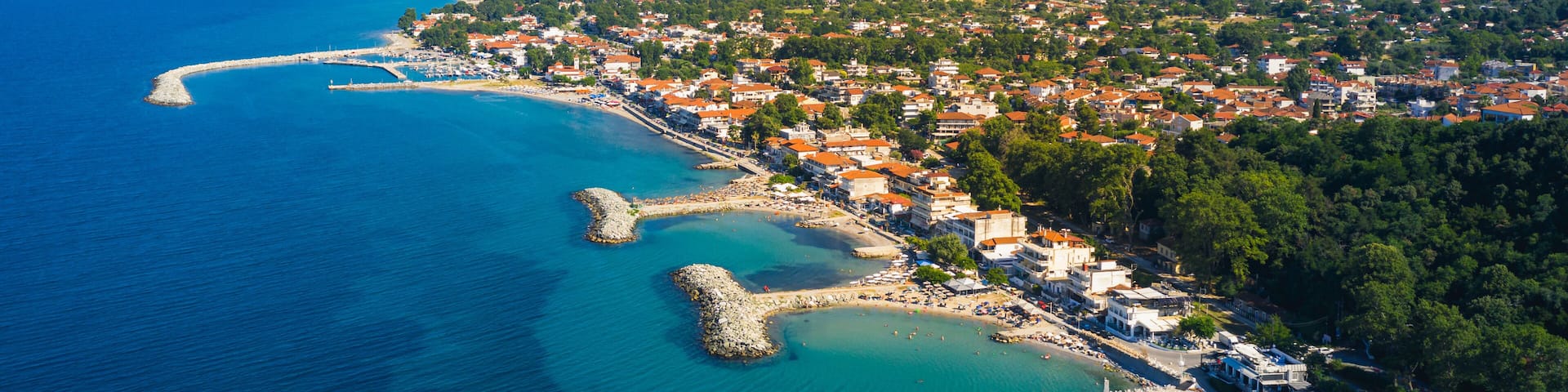A coastal town with a clear blue sea, a winding harbor, and a mountainous backdrop.