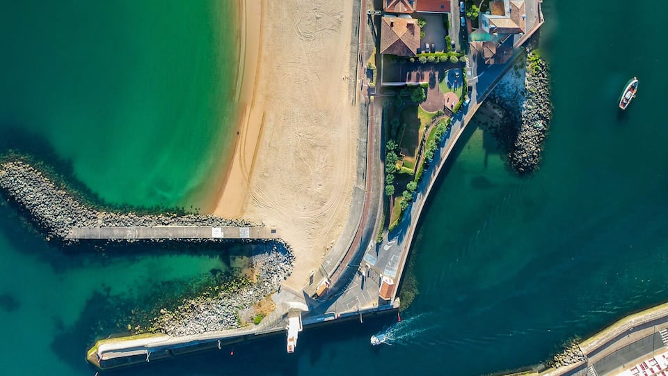 An aerial view of a coastal town with a beach, marina, and dense urban area.