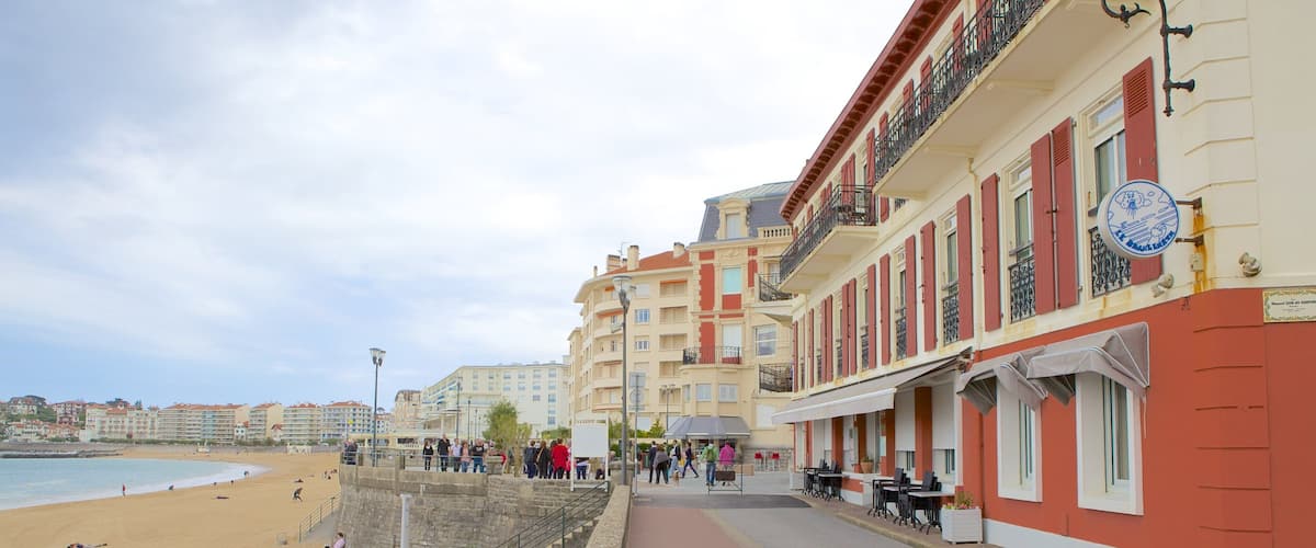 A beach with people sunbathing and walking along a promenade lined with buildings.