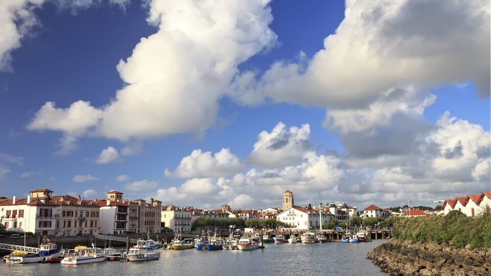 A harbor with boats, buildings, and a tower under a partly cloudy sky.