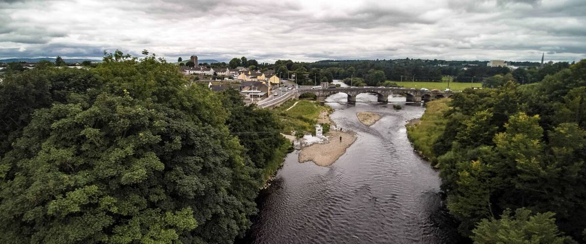 A river flowing through a town with a bridge and dense greenery on both sides.