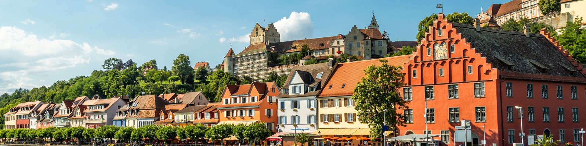 Eine Hafenstadt mit bunten Häusern, ein Boot an der Anlegestelle und eine Burg auf einem Hügel im Hintergrund.
