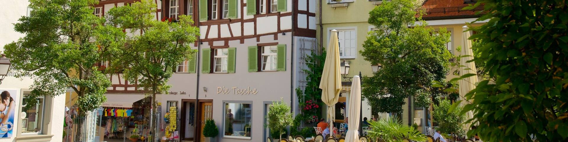 A European town square with traditional half-timbered houses, outdoor cafes, and a shop named 'Die Tasse'.