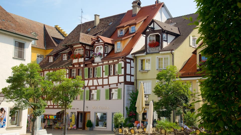 A European town square with traditional half-timbered houses, outdoor cafes, and a shop named 'Die Tasse'.