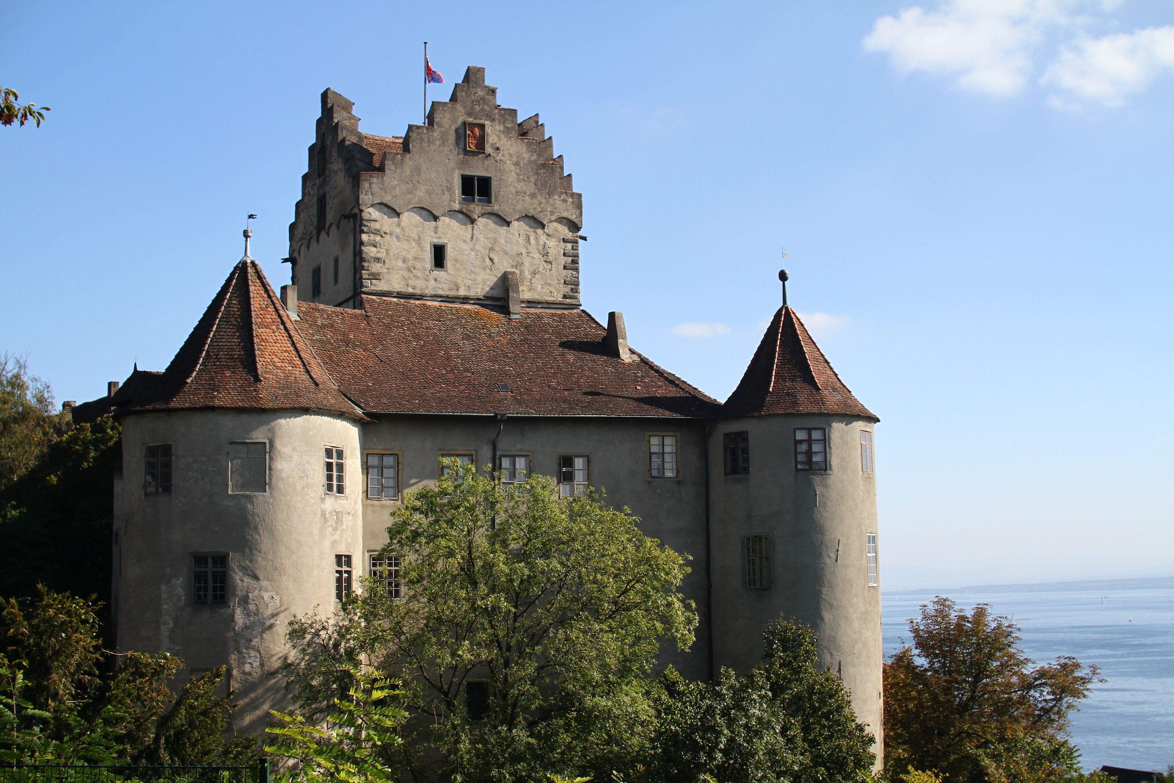 A castle with a tower, surrounded by trees and overlooking a body of water.