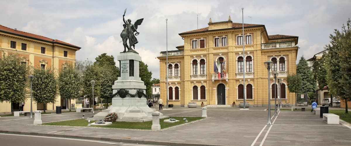 A square with a statue, a yellow building, and trees.