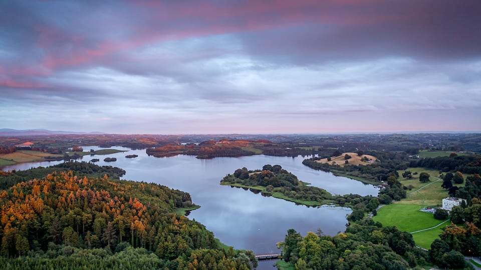 A lake surrounded by forested hills, a bridge, and a white building.