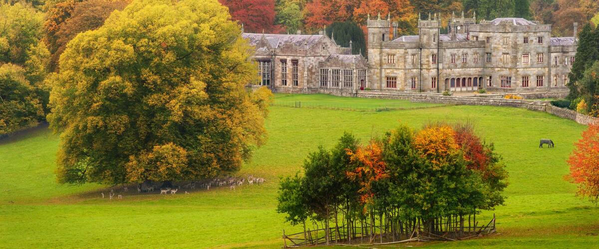 A historic stone building surrounded by autumn-colored trees and a green field with grazing animals.