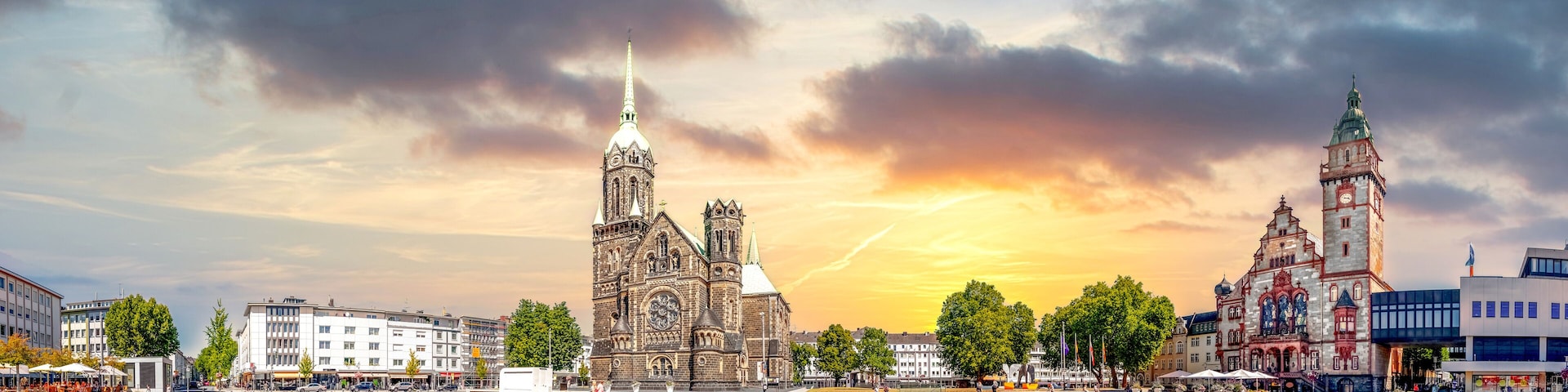 Uma igreja histórica com uma torre alta, um campanário e um edifício moderno com fachada colorida.