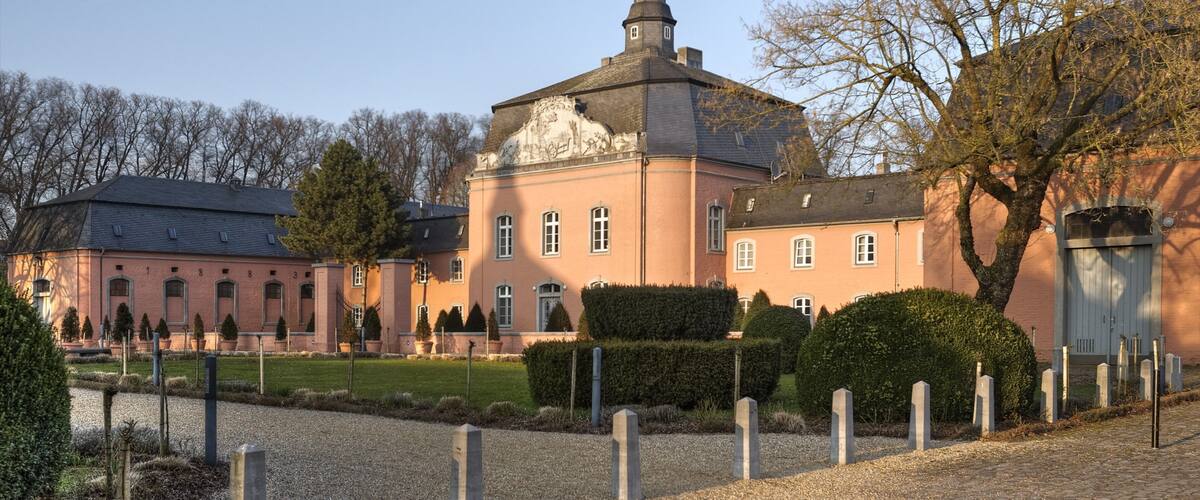 A large pink building with a tower, surrounded by a gravel path and trimmed hedges.