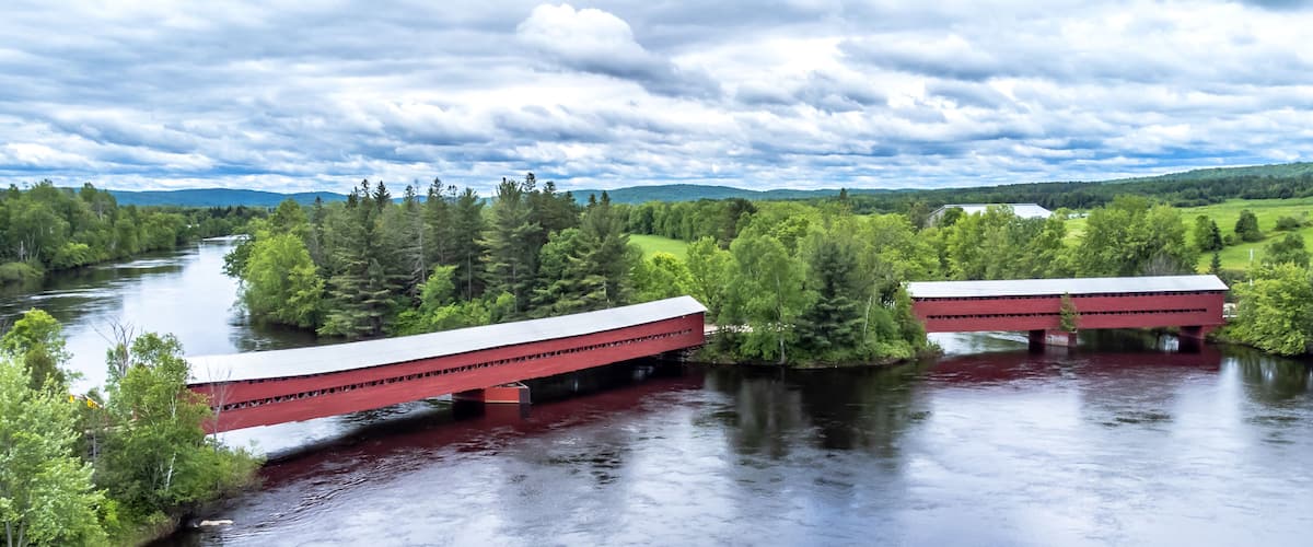 A red covered bridge over a river, surrounded by lush greenery and hills in the background.