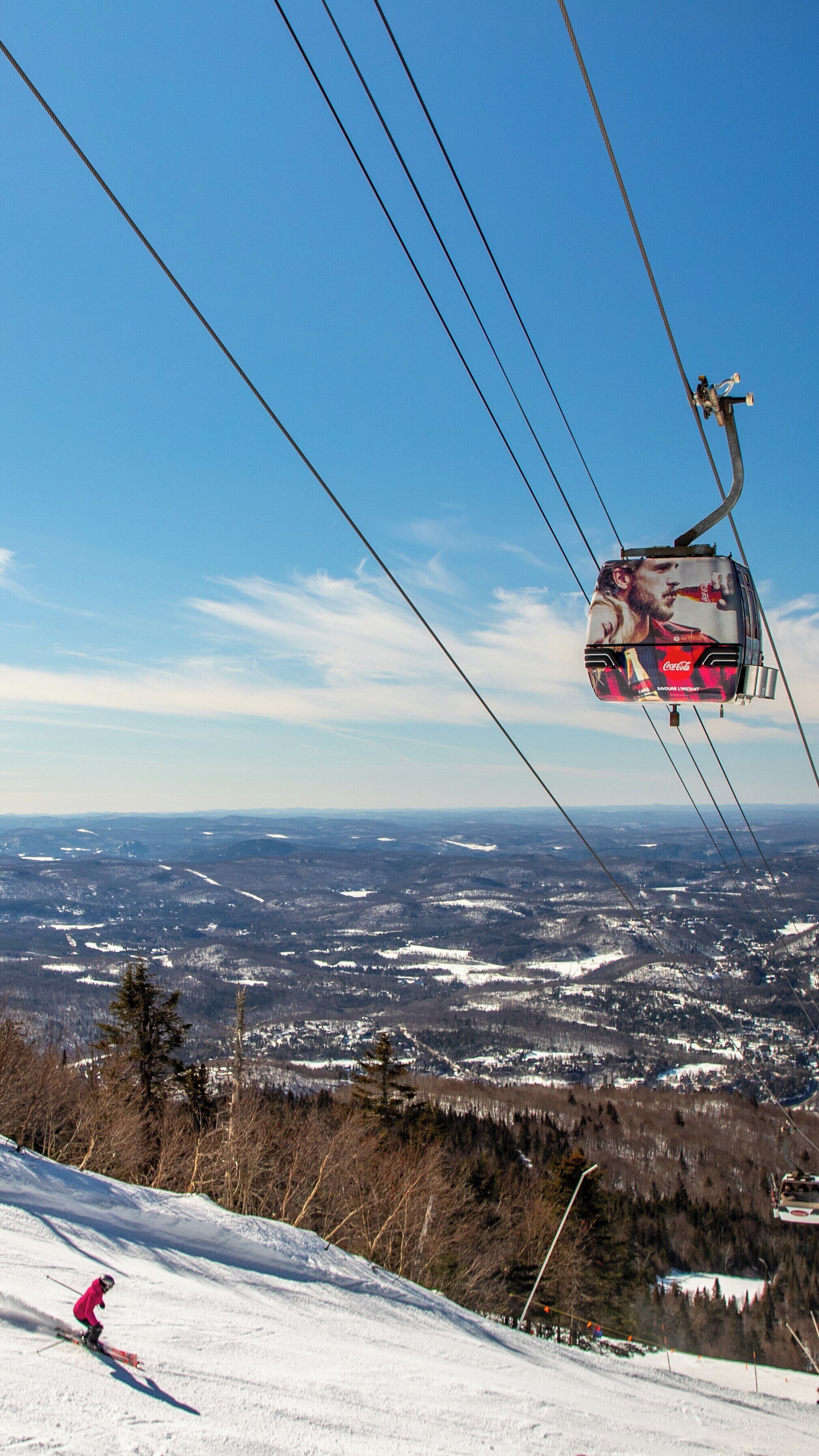 Skiing down the slopes while the Express Gondola travels above in Mont-Tremblant, Quebec under a clear blue sky