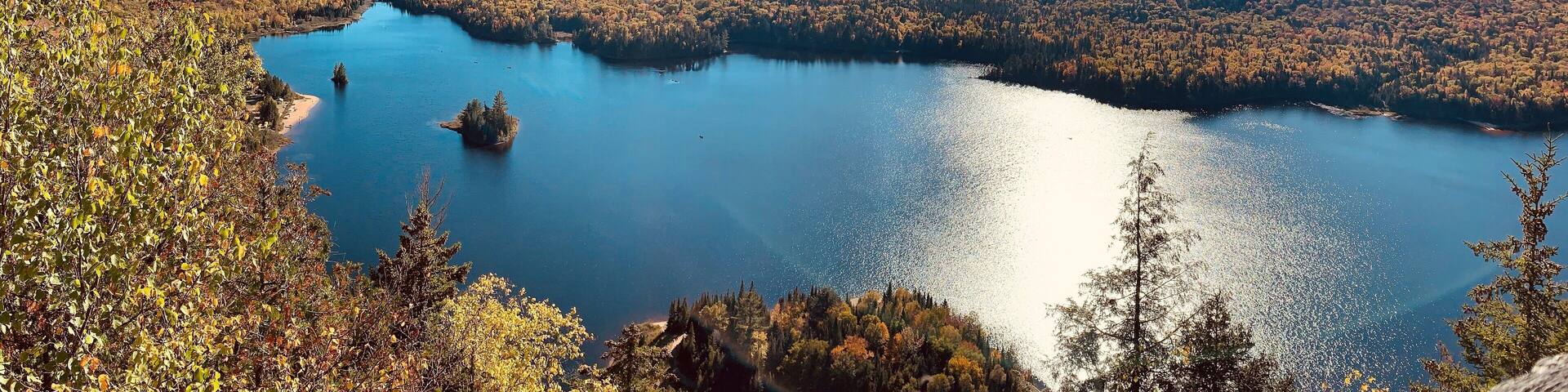 A lake surrounded by autumn-colored forests and distant mountains under a clear sky.