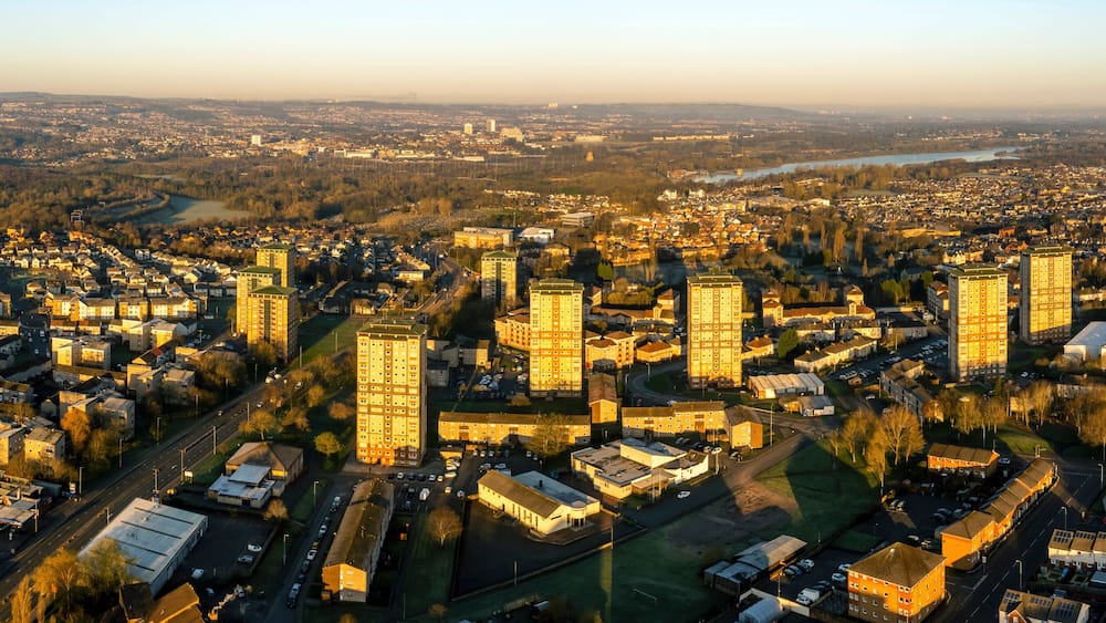 An aerial view of a cityscape with dense urban development, a river, and surrounding greenery.