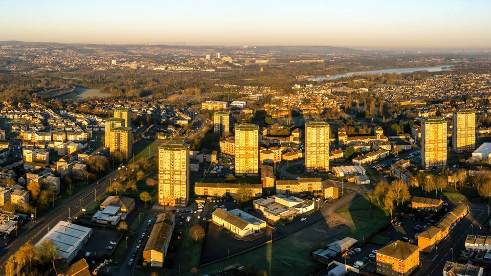 An aerial view of a cityscape with dense urban development, a river, and surrounding greenery.