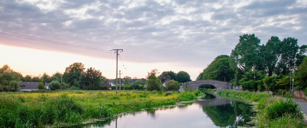 A calm river with a stone bridge, surrounded by lush greenery and trees.