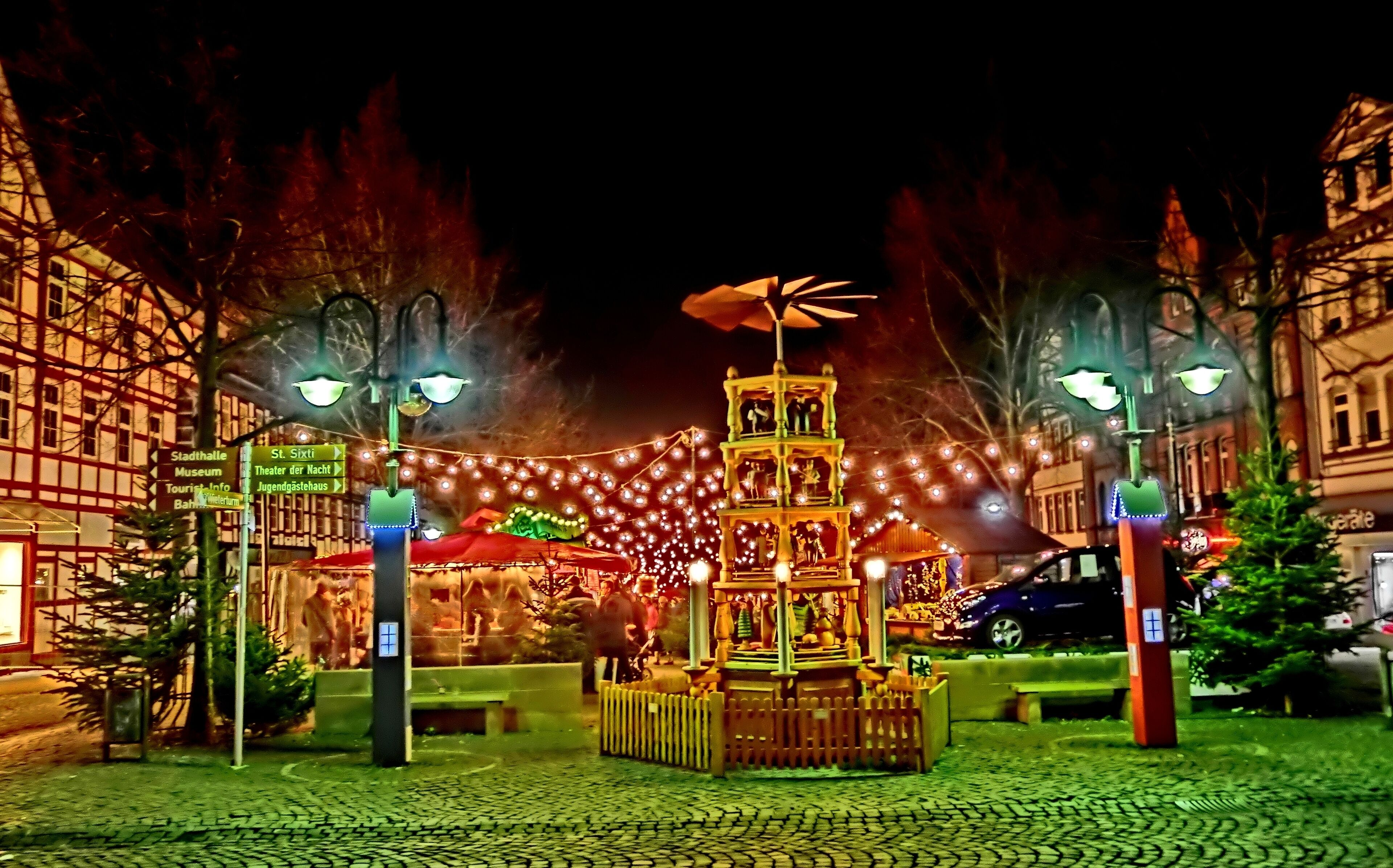 Una escena nocturna con una torre iluminada, farolas y un mercado navideño al fondo.