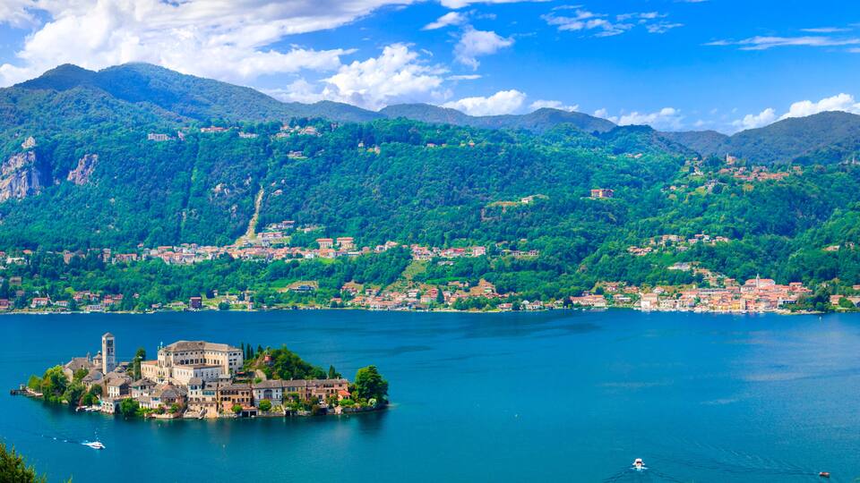 A lake surrounded by mountains, a small island with a church, and a town in the background.