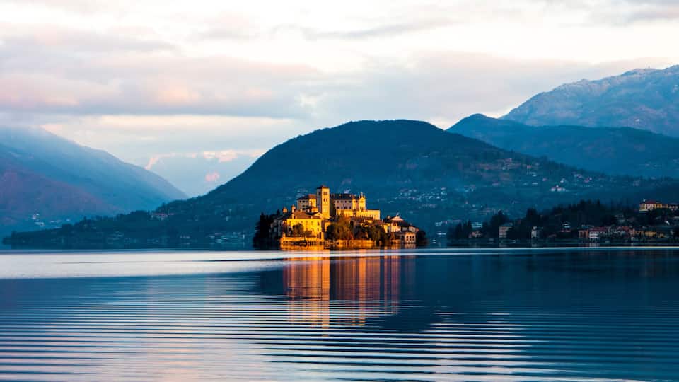 A serene lake with a historic building on an island, surrounded by mountains.