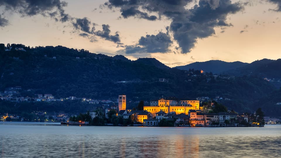 A lakeside town with illuminated buildings and a prominent tower, surrounded by hills.