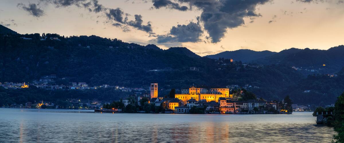 A lakeside town with illuminated buildings and a prominent tower, surrounded by hills.