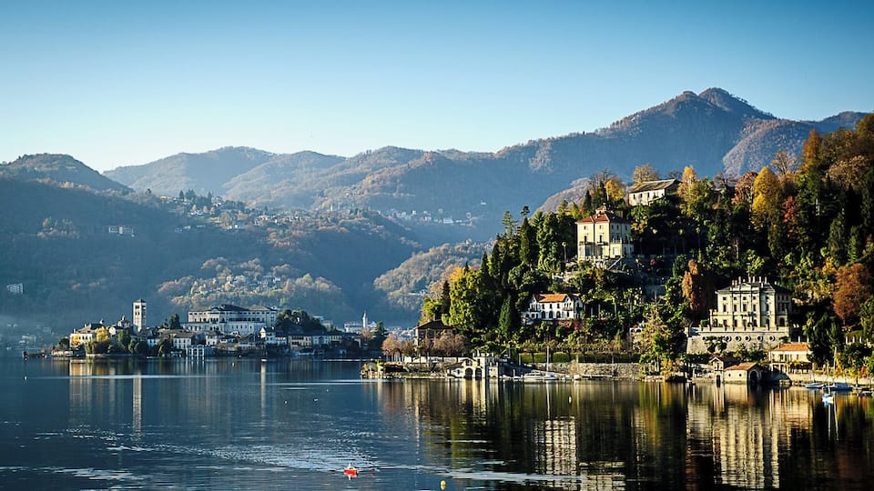A calm lake with a small boat, surrounded by mountains and buildings on the shore.