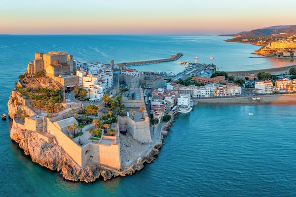 Un pueblo costero con un castillo amurallado, un puerto deportivo y una playa.