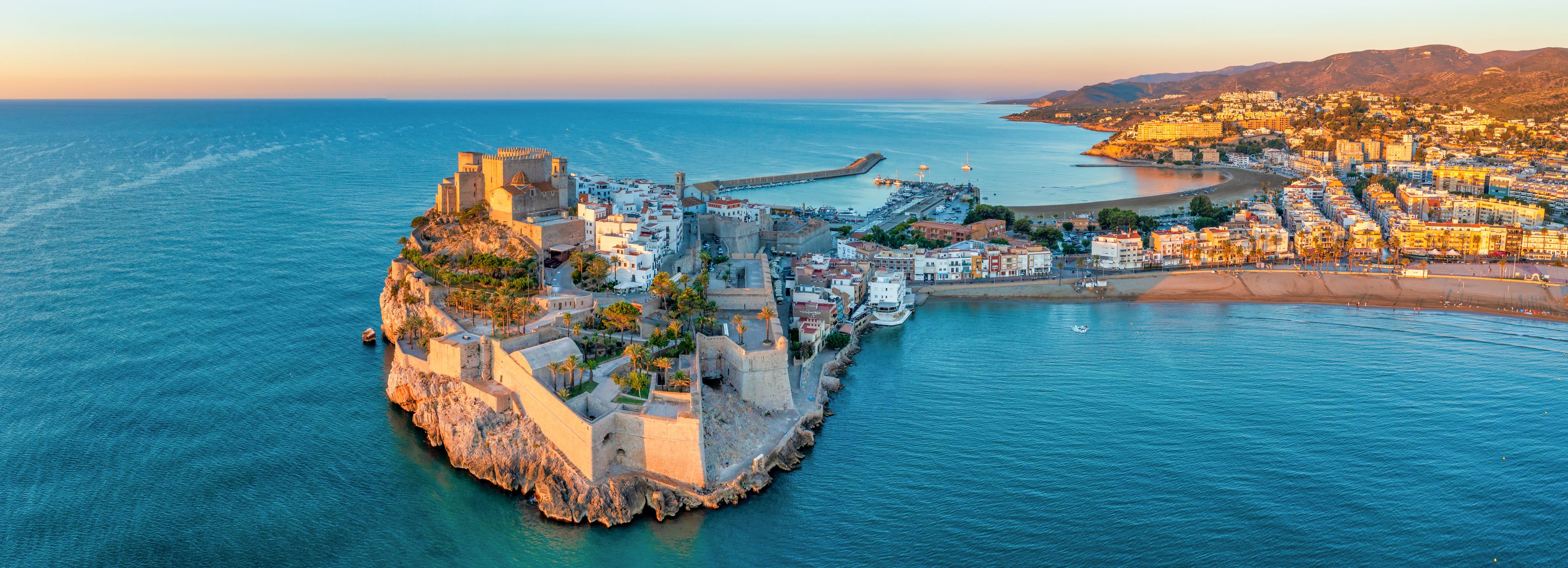 A coastal town with a fortified castle, a marina, and a beach.