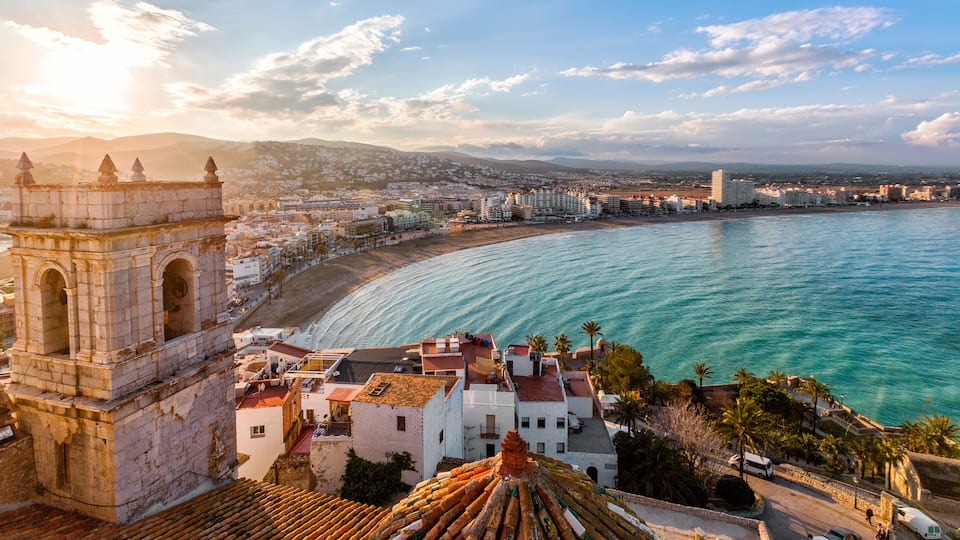 A coastal cityscape with a prominent tower, a beach, and a clear view of the ocean.