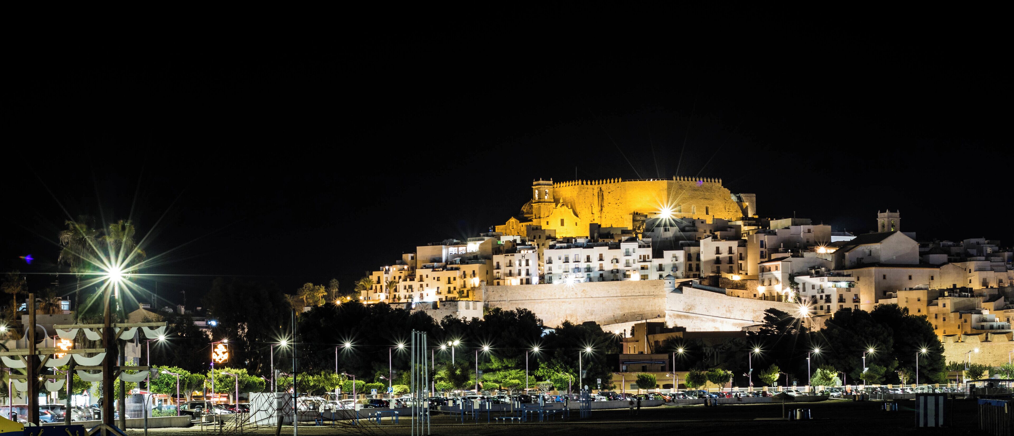 A historic walled city at night with illuminated buildings and a prominent fortress on a hill.