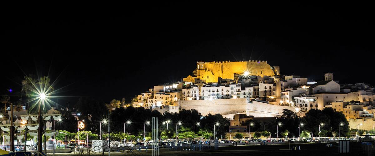 A historic walled city at night with illuminated buildings and a prominent fortress on a hill.