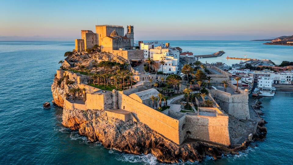 A coastal town with a historic fortification, a lighthouse, and a clear view of the sea.