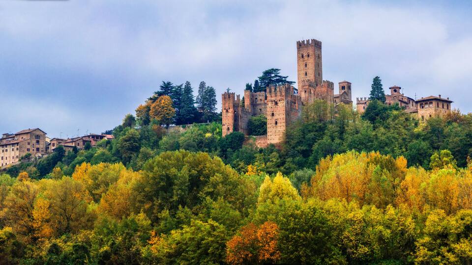 A historic castle on a hill surrounded by autumn-colored trees.