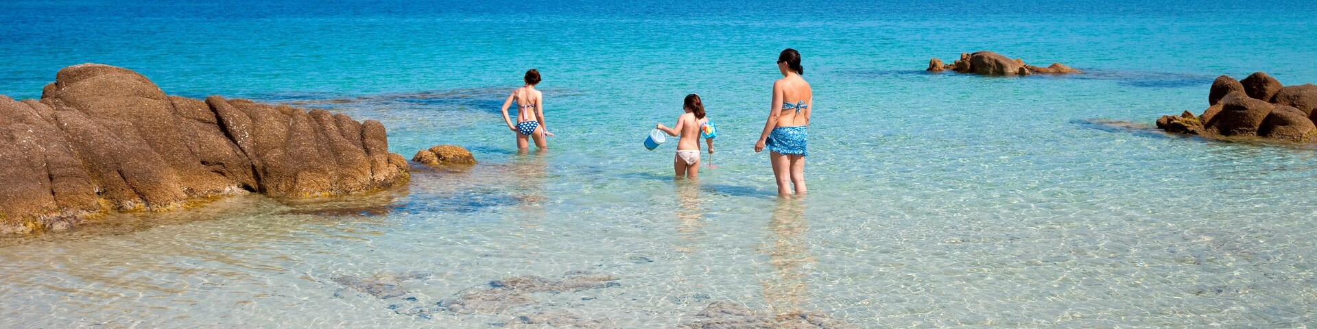 Uma praia com águas turquesa cristalinas, formações rochosas e montanhas ao longe.