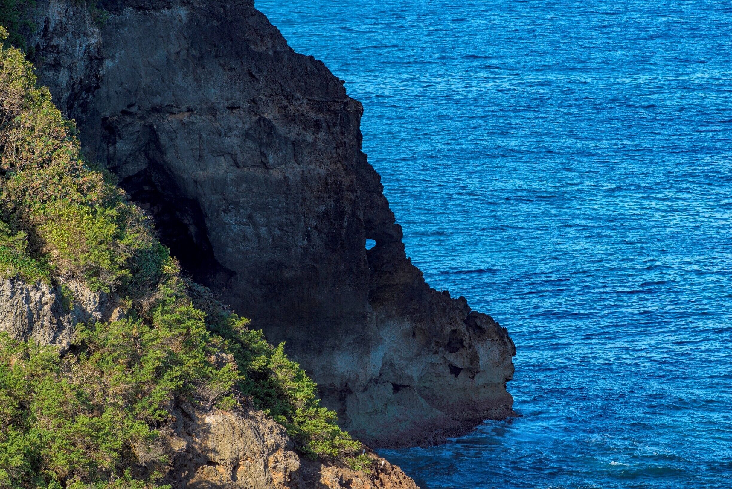 A rugged cliff with a cave opening, overlooking a deep blue ocean.