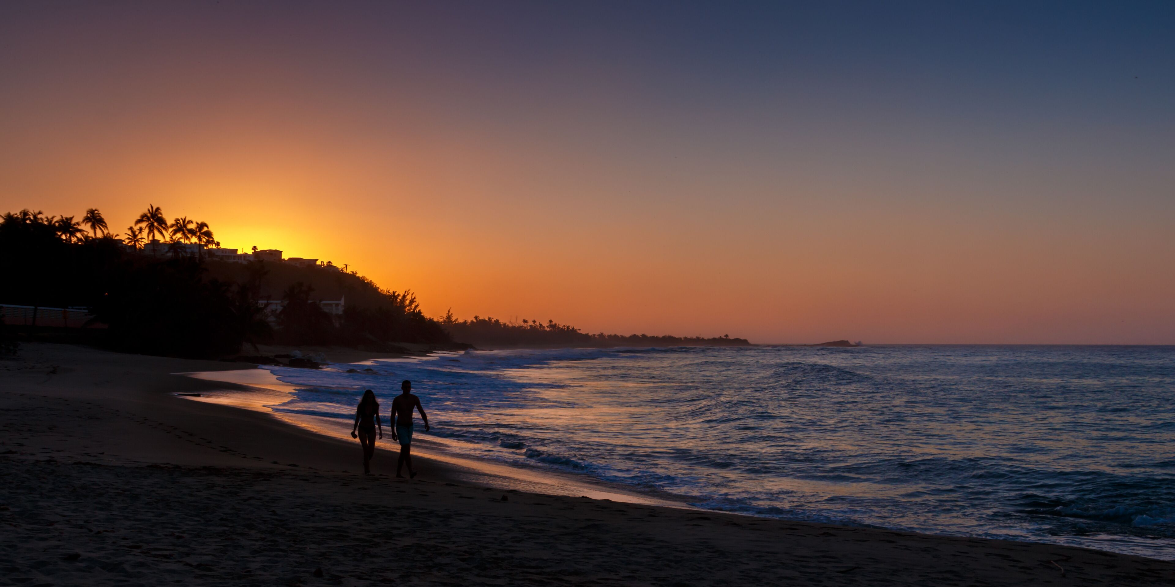 A beach at sunset with two people walking along the shore.