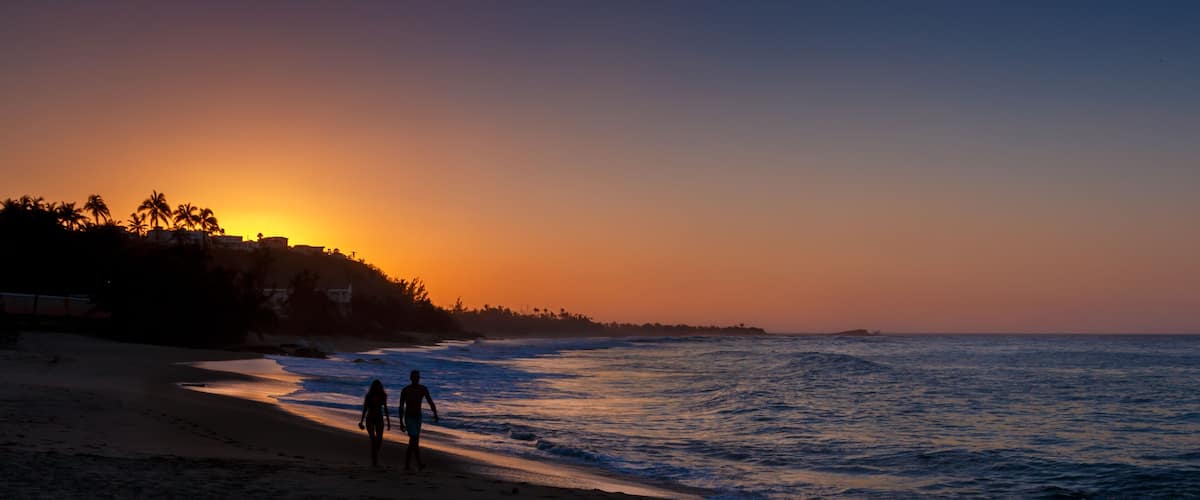 A beach at sunset with two people walking along the shore.