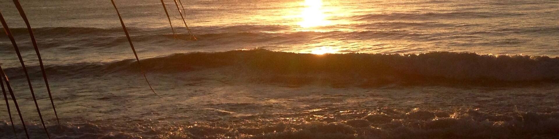 A sunset over the ocean with waves and a sailboat in the distance.