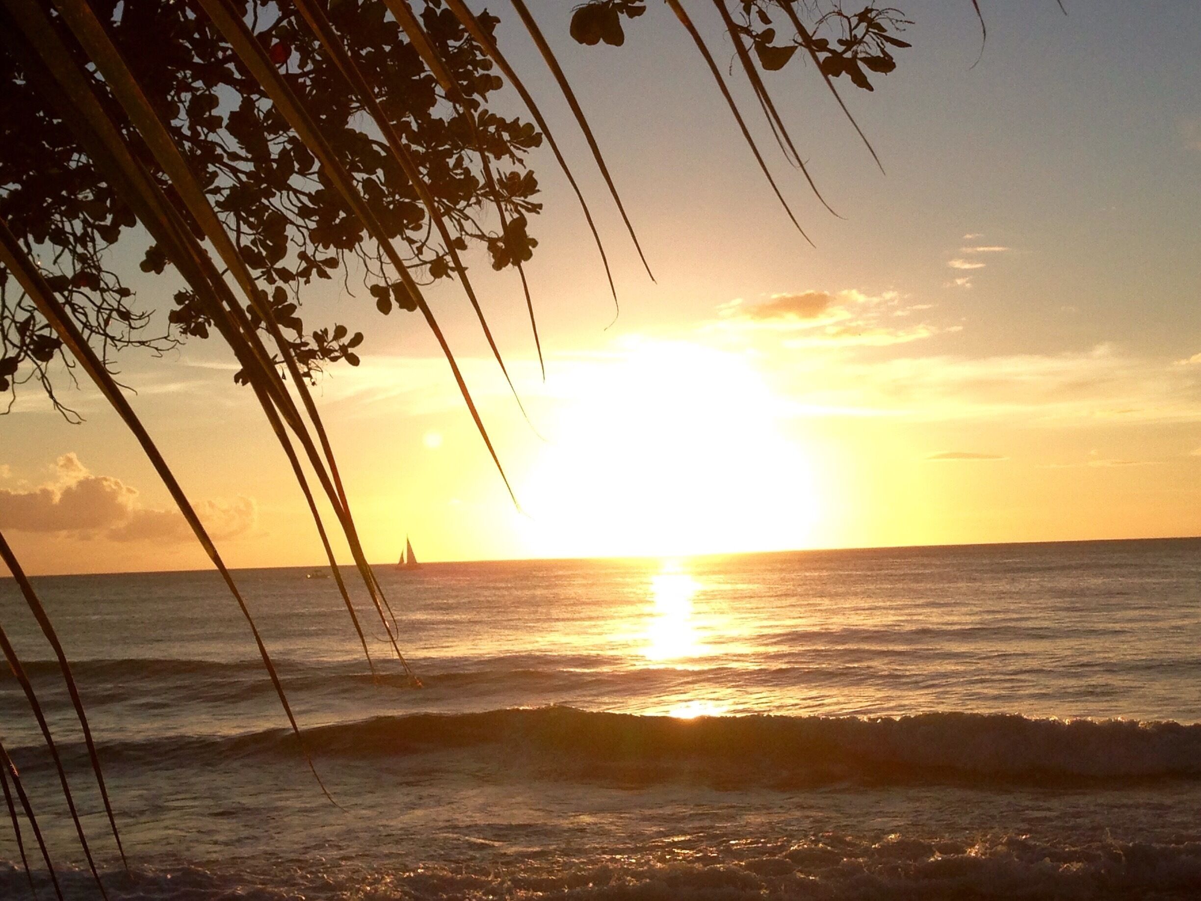 A sunset over the ocean with waves and a sailboat in the distance.