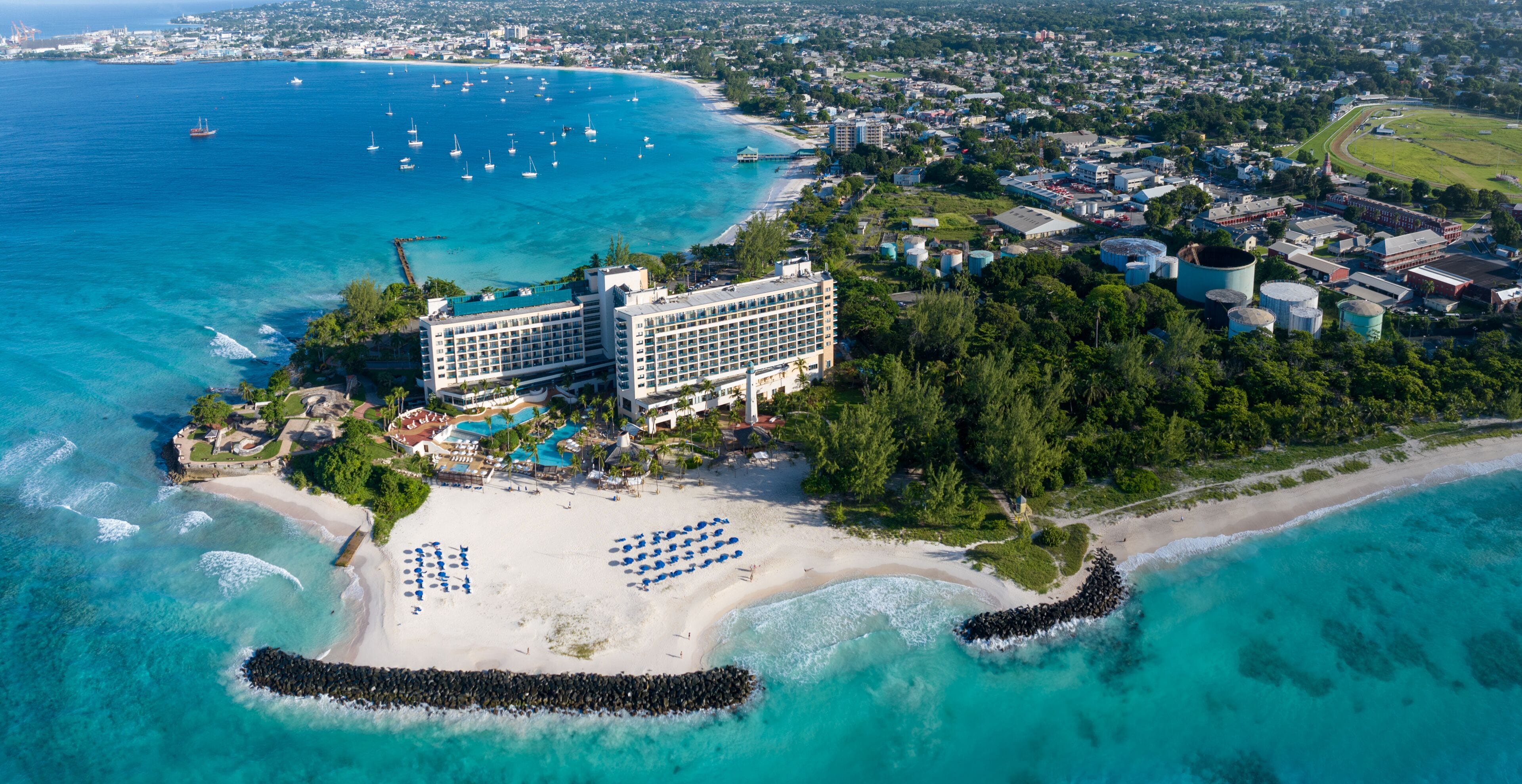 An aerial view of a coastal resort with a large hotel, beach, and marina.