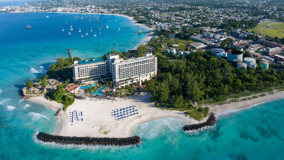An aerial view of a coastal resort with a large hotel, beach, and marina.