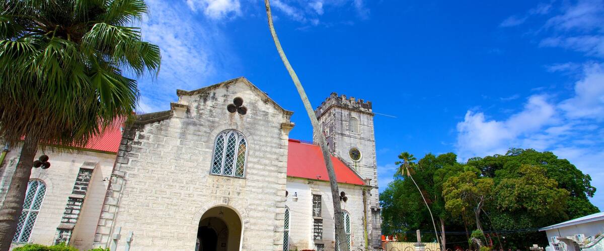 A historic church with a red roof and a clock tower, surrounded by lush greenery and palm trees.