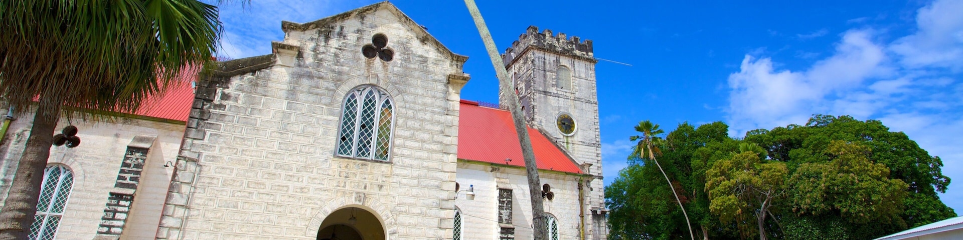 A historic church with a red roof and a clock tower, surrounded by lush greenery and palm trees.