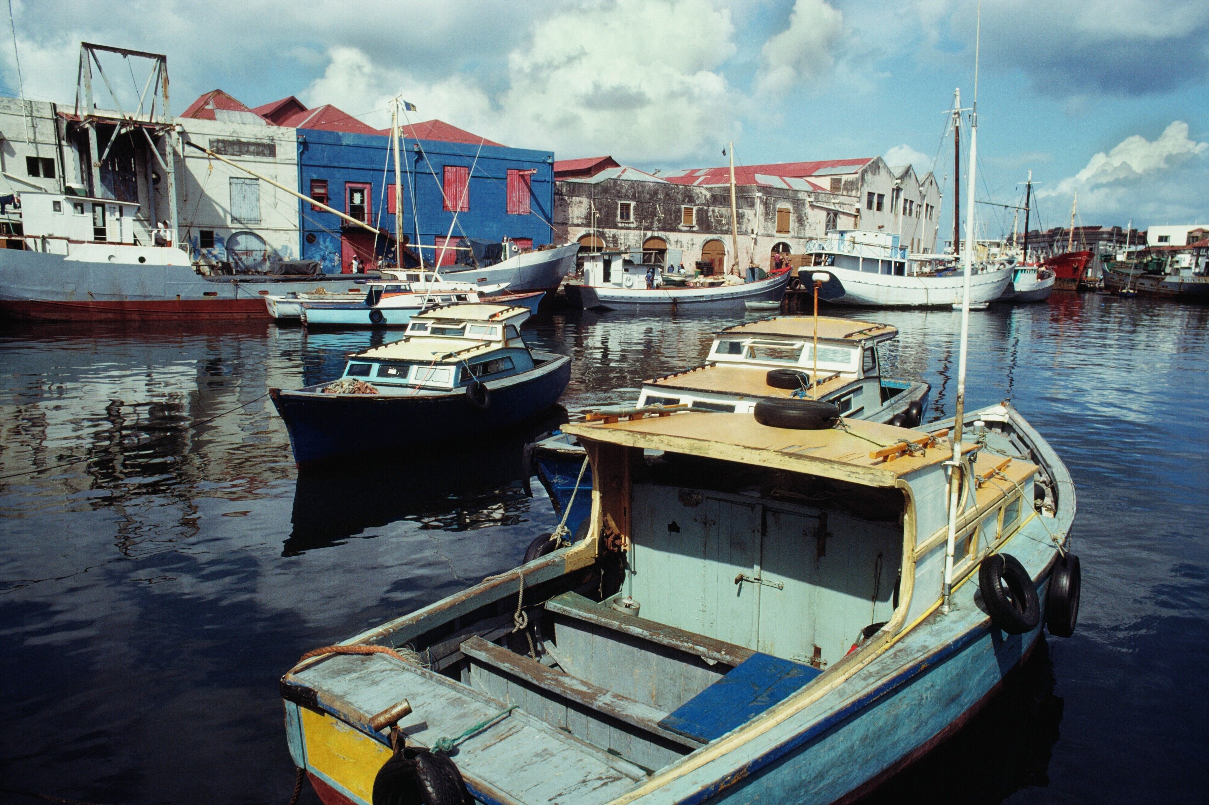 A harbor with several boats docked, a blue building with red shutters, and a white building with a red roof.