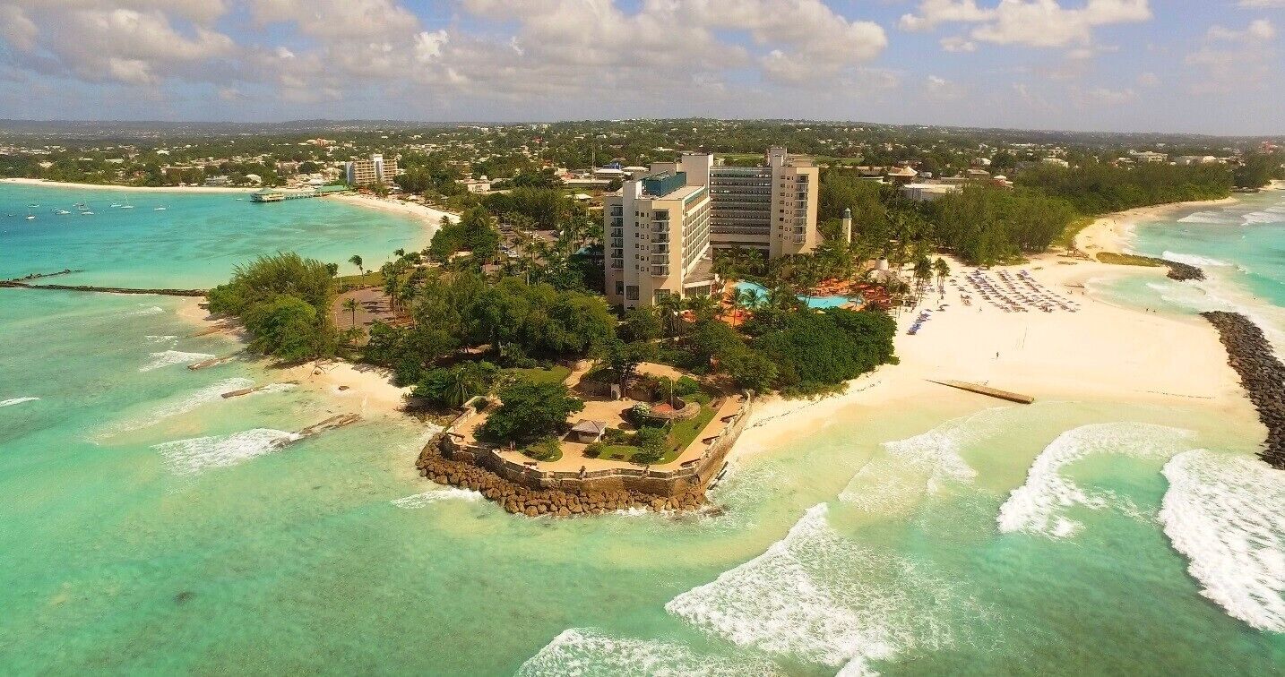 A coastal resort with a beach, clear turquoise waters, and a central building surrounded by greenery.