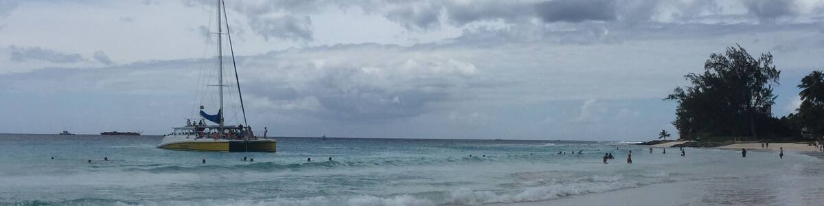 Ein Strand mit einem Segelboot im Wasser und badenden Menschen.