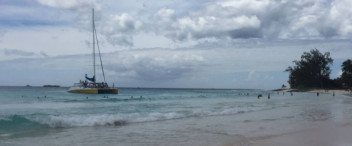 A beach with a sailboat in the water and people swimming.